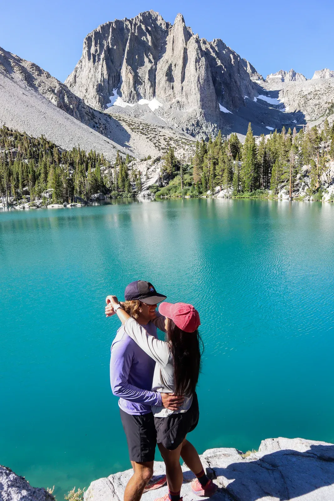 Brendon and Kaylee kissing in front of a turquoise lake under a granite peak.