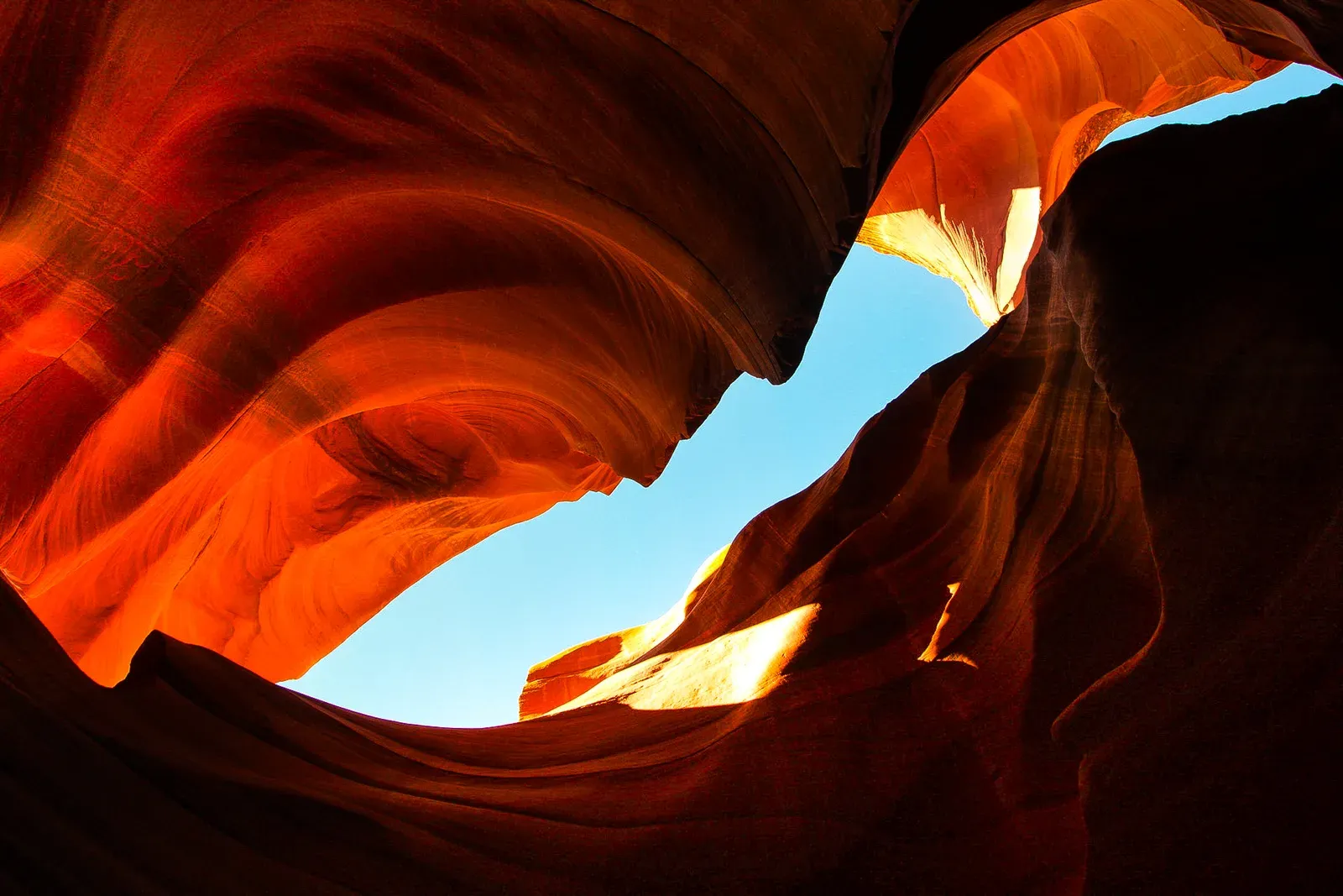 Looking up through a glowing orange slot canyon to blue sky.