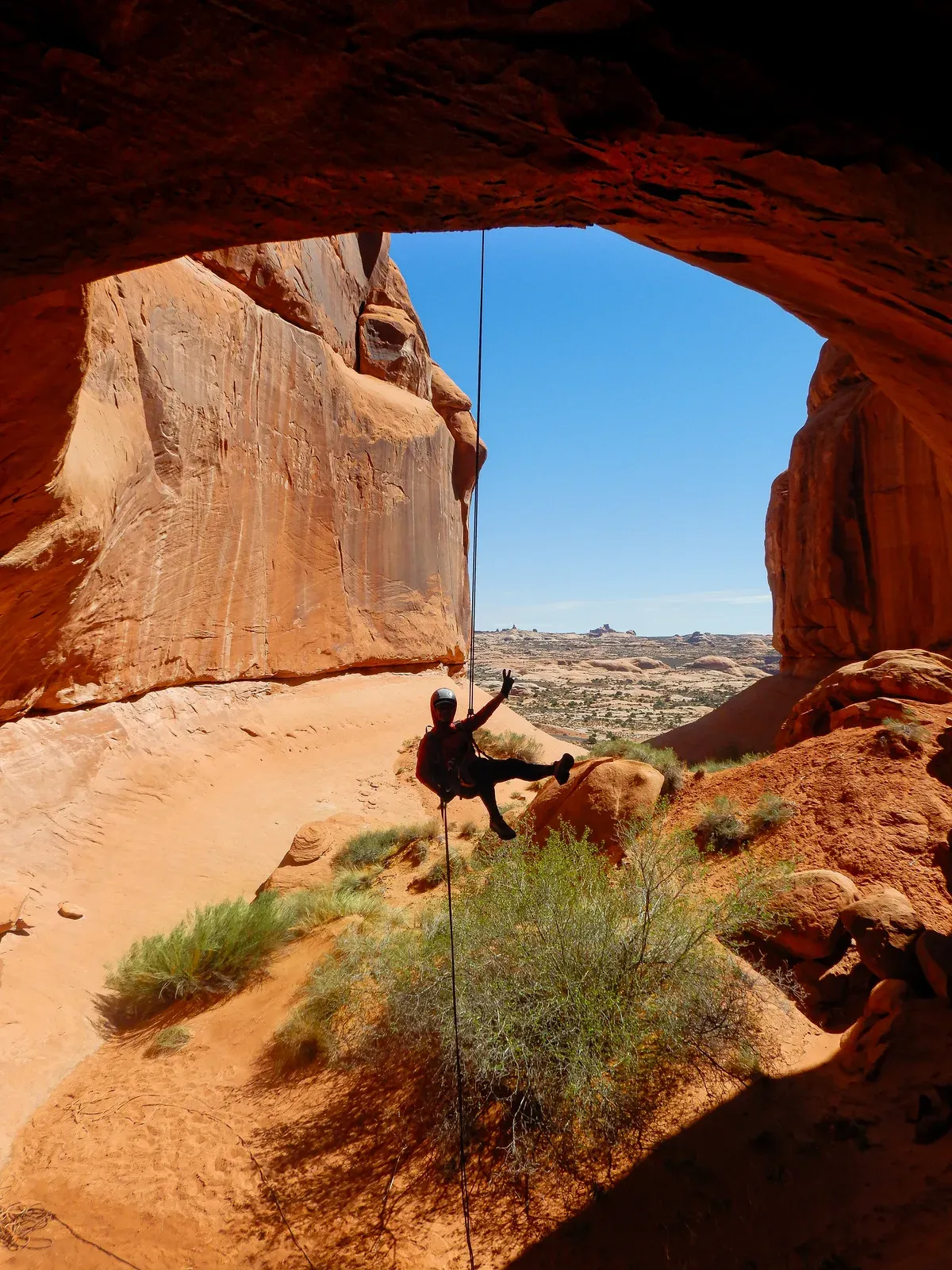 A climber rappelling out of a sandstone window over the desert.