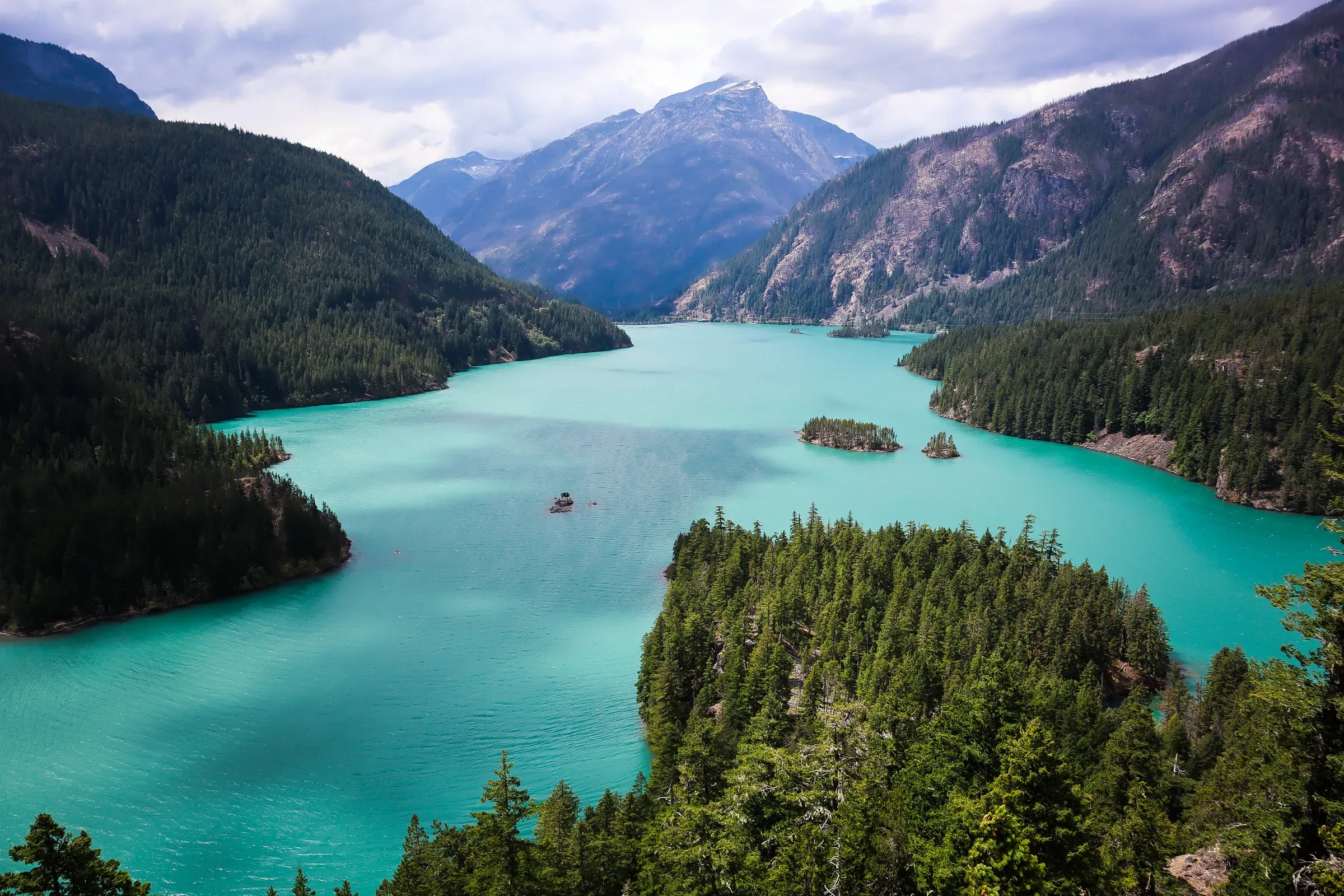 A turquoise lake with islands between forested mountains.