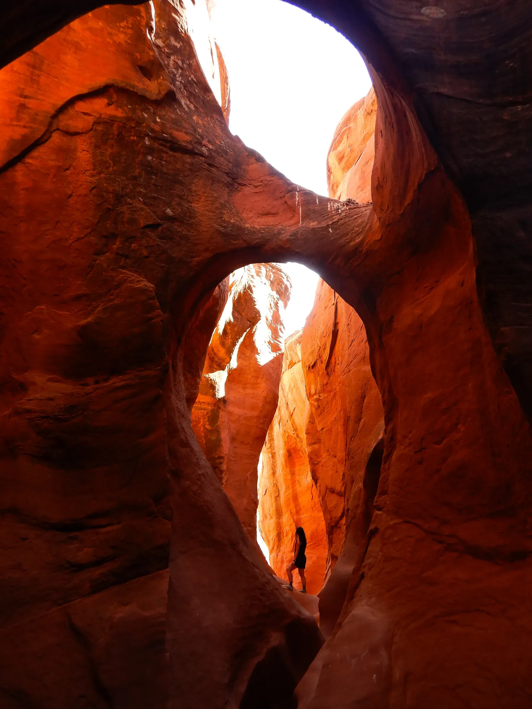 A double arch inside a deep red slot canyon, a tiny person below.