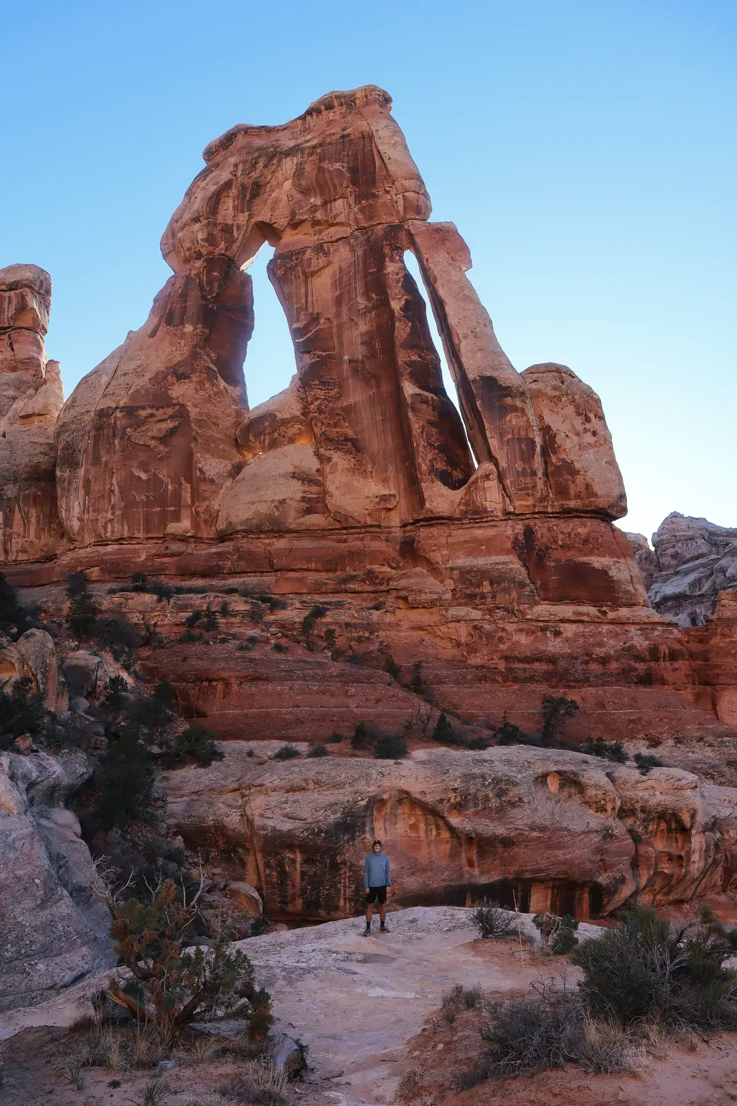 A tall slotted sandstone arch on a ridge, a tiny hiker below.