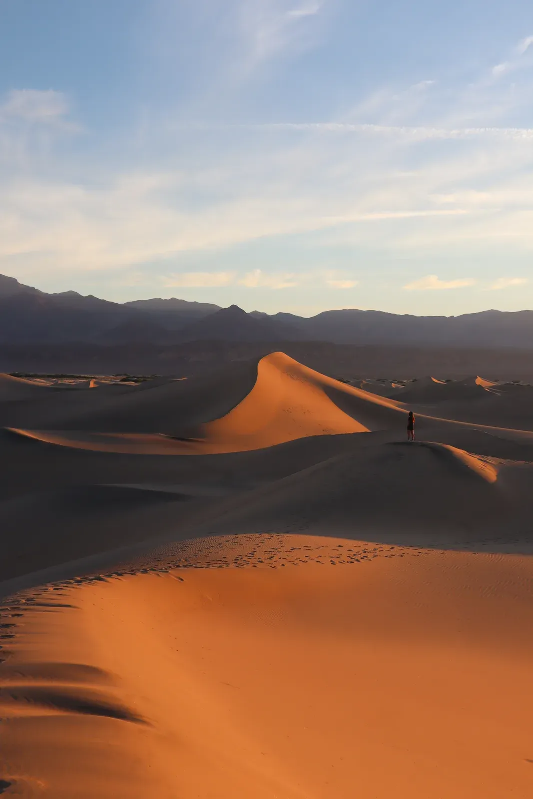 A lone hiker on a sweeping sand dune ridge.