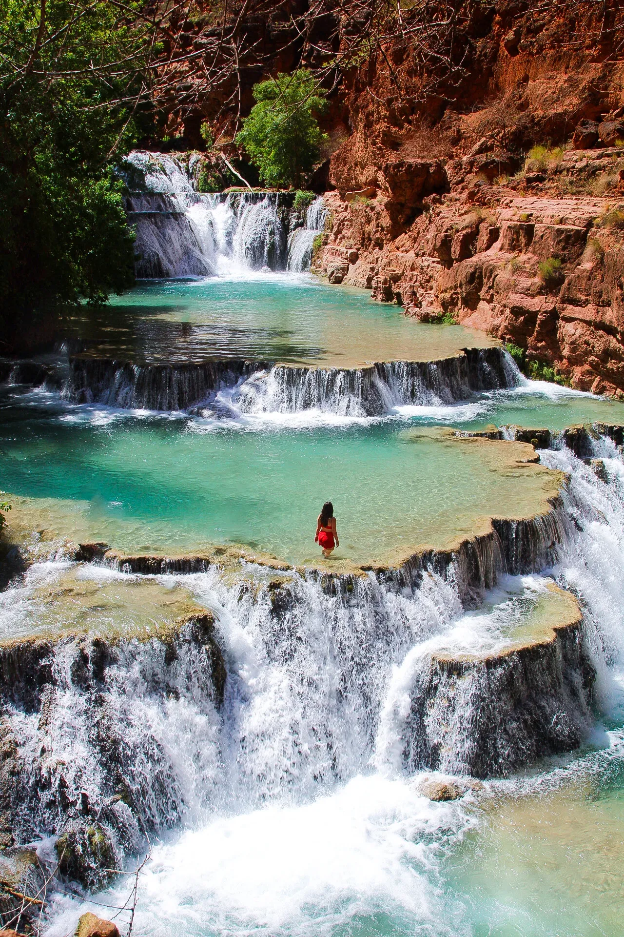 Turquoise travertine pools and cascades, a woman in red on a ledge.