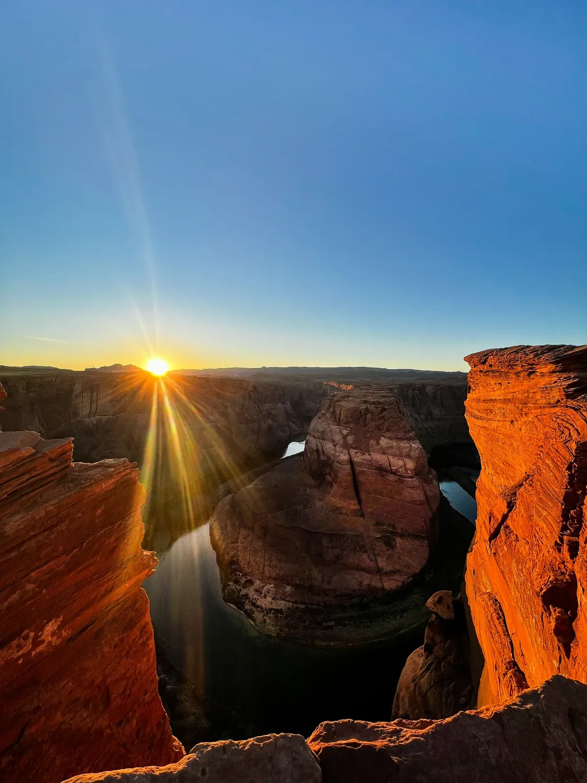 A sunburst over a deep river bend in a red canyon.