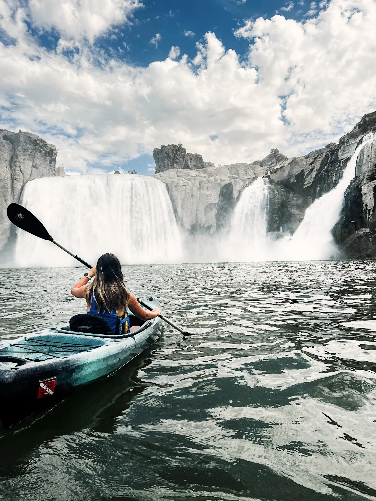 A kayaker paddling toward a wide waterfall.