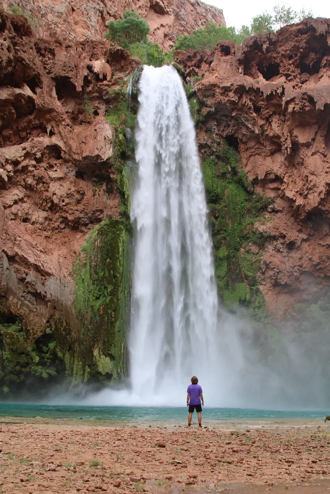 A tall waterfall into a turquoise pool, one person at the edge.
