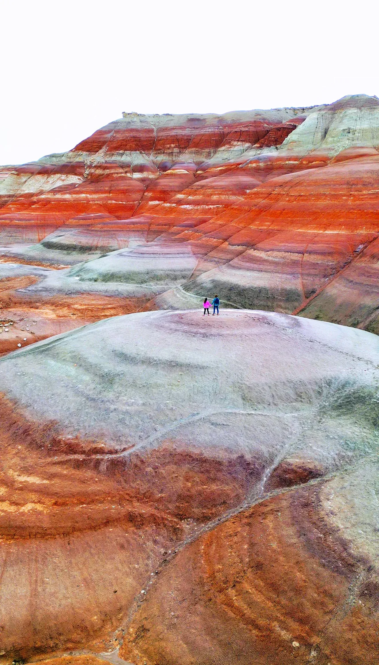 Drone view of striped red and white hills with two tiny people.