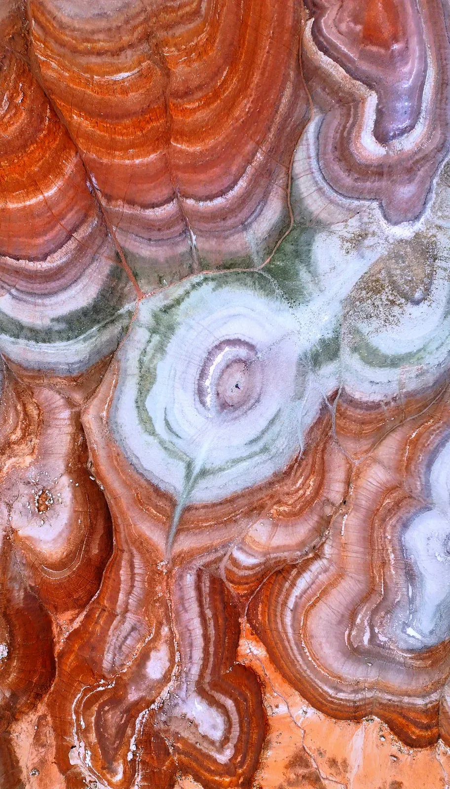 Drone view of concentric red, white and green rock swirls.