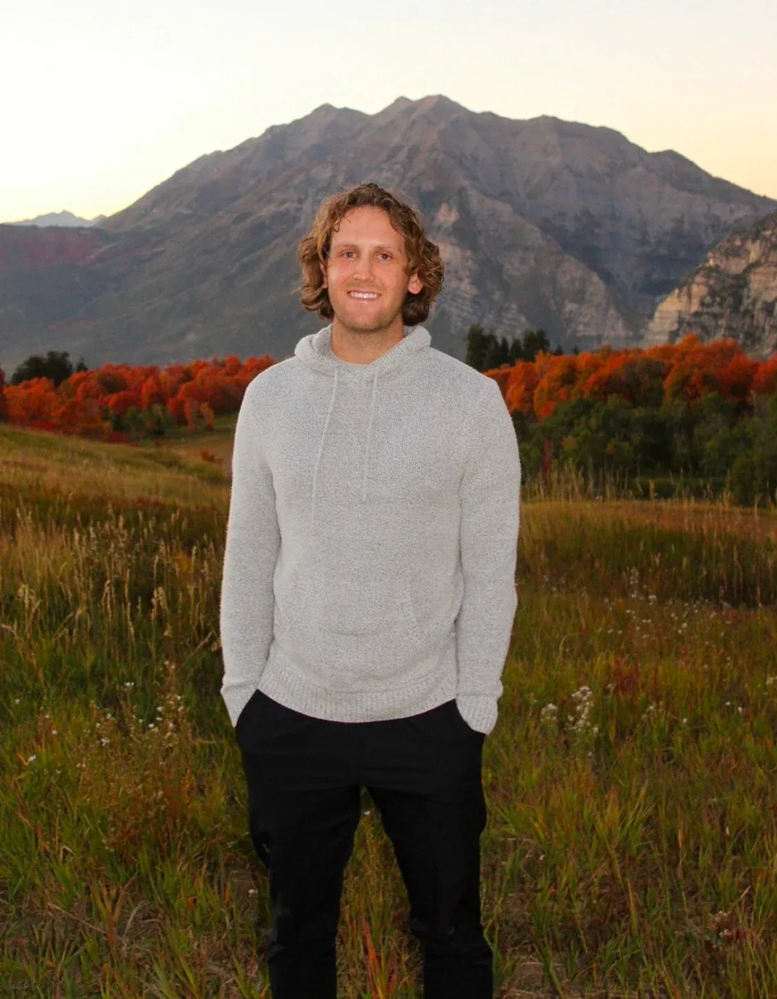 Brendon Jensen standing in a field below Mt. Timpanogos in the fall.