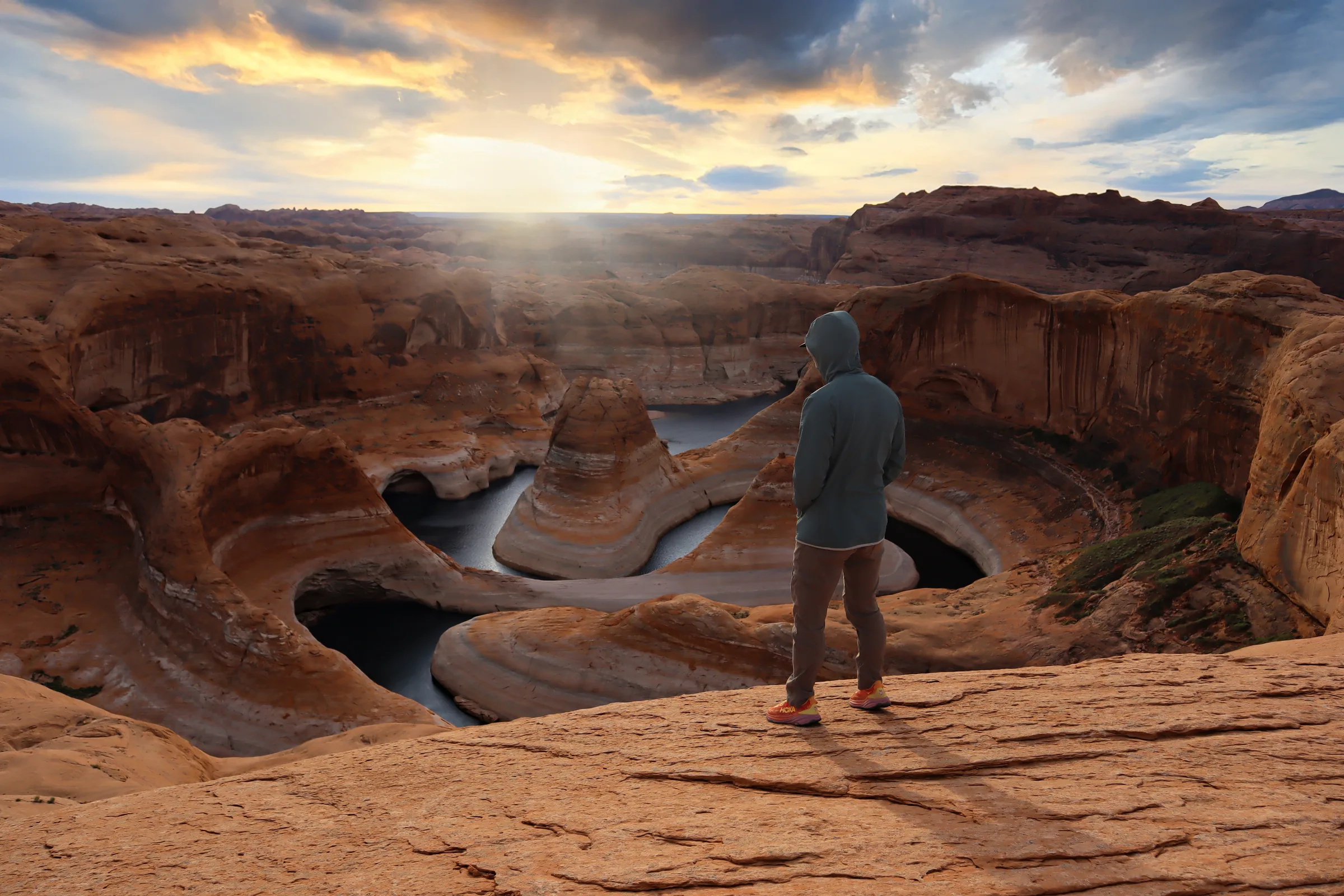 Brendon at the rim of Reflection Canyon, water winding far below under sunbeams.