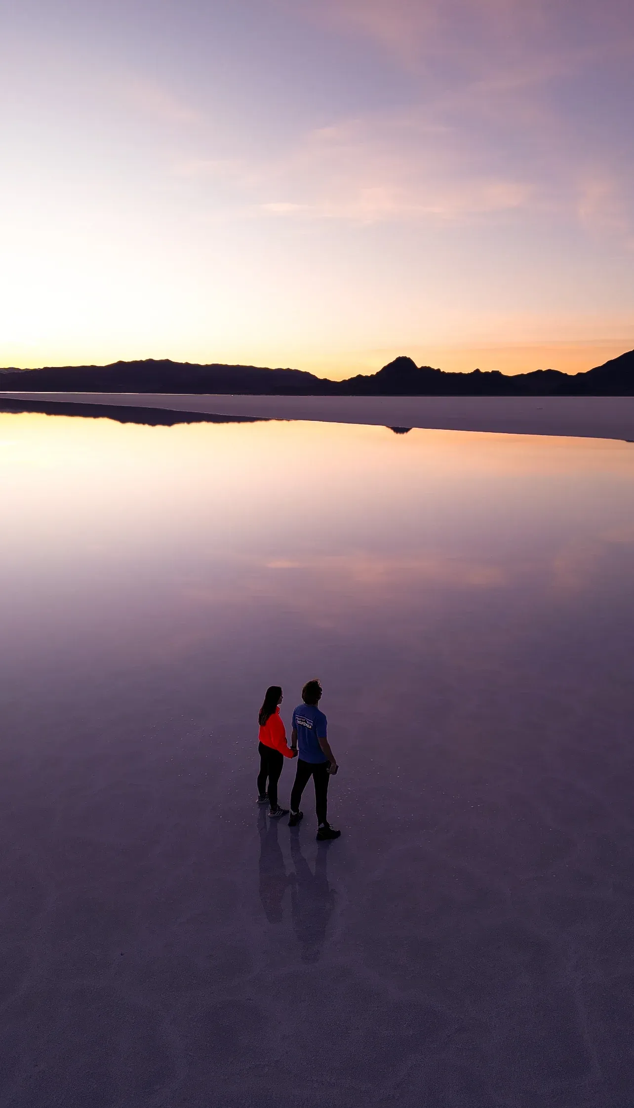 Brendon and Kaylee walking on a mirror-like salt flat at sunset.