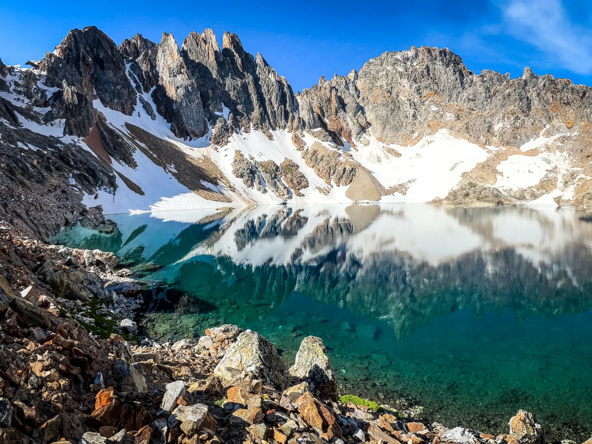 Jagged snowy peaks mirrored in a green alpine lake.