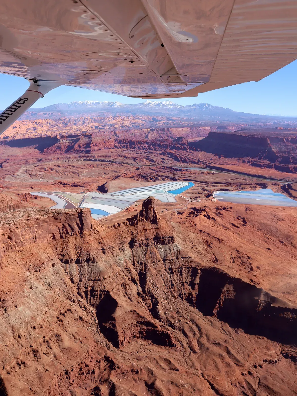 The view from a small plane's wing over red canyons and blue ponds.