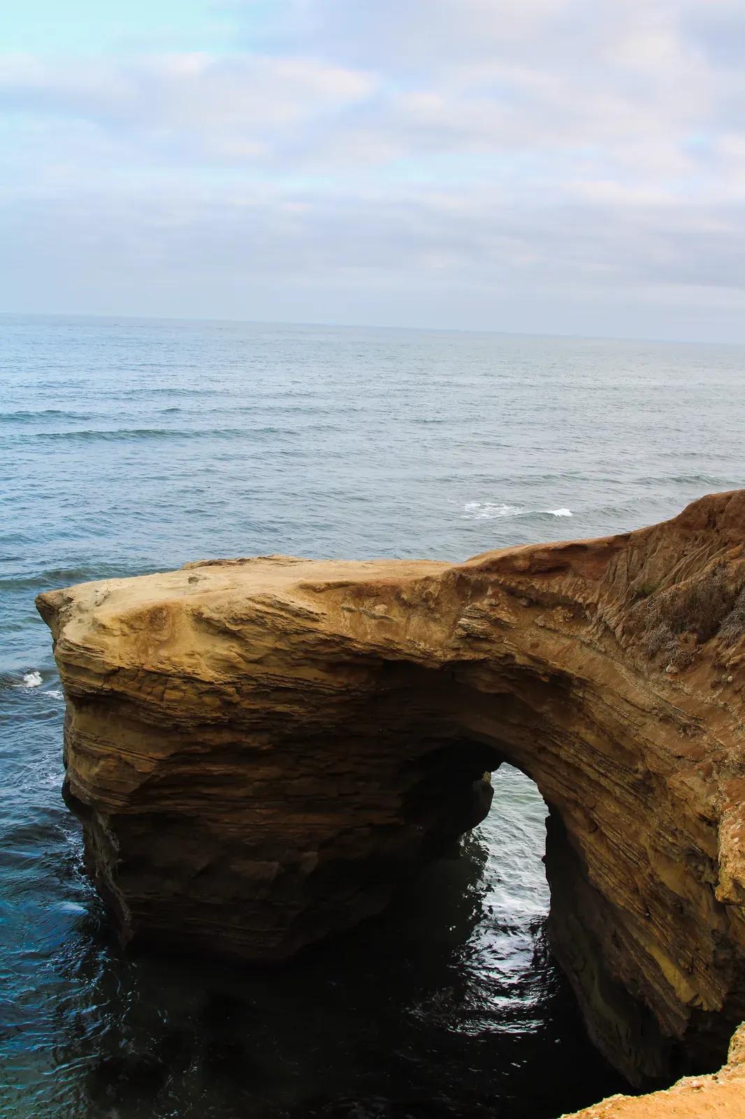 A sandstone sea arch over a calm ocean.