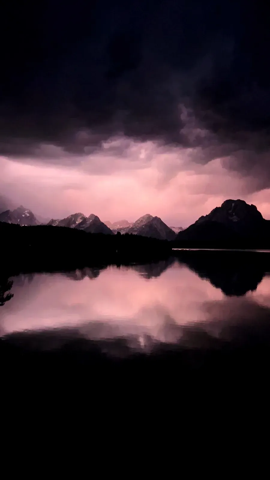 Dark storm clouds lit pink over jagged peaks, mirrored in a still lake.