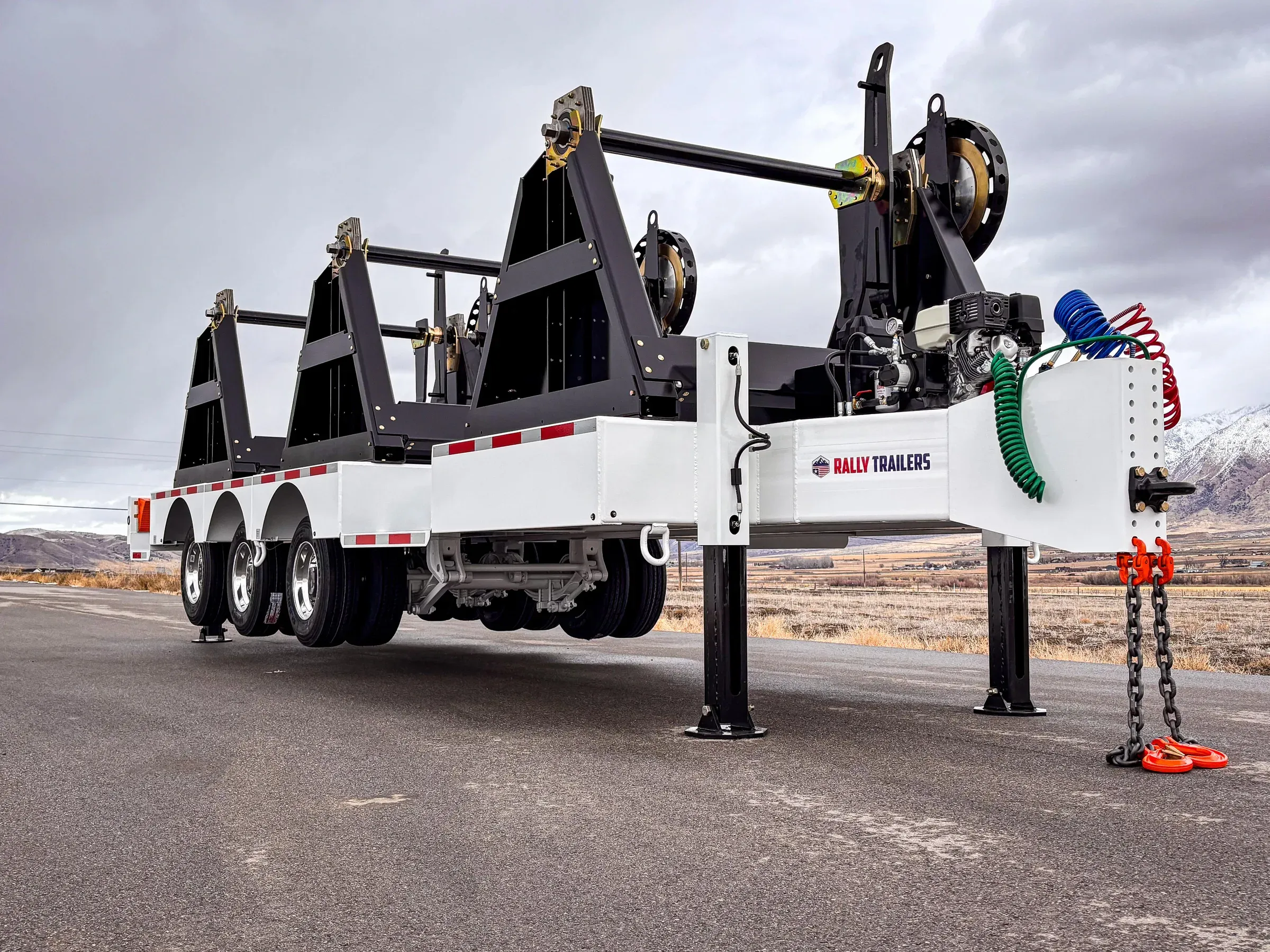 A white triple-axle Rally reel trailer parked on a road, photographed from a low angle.