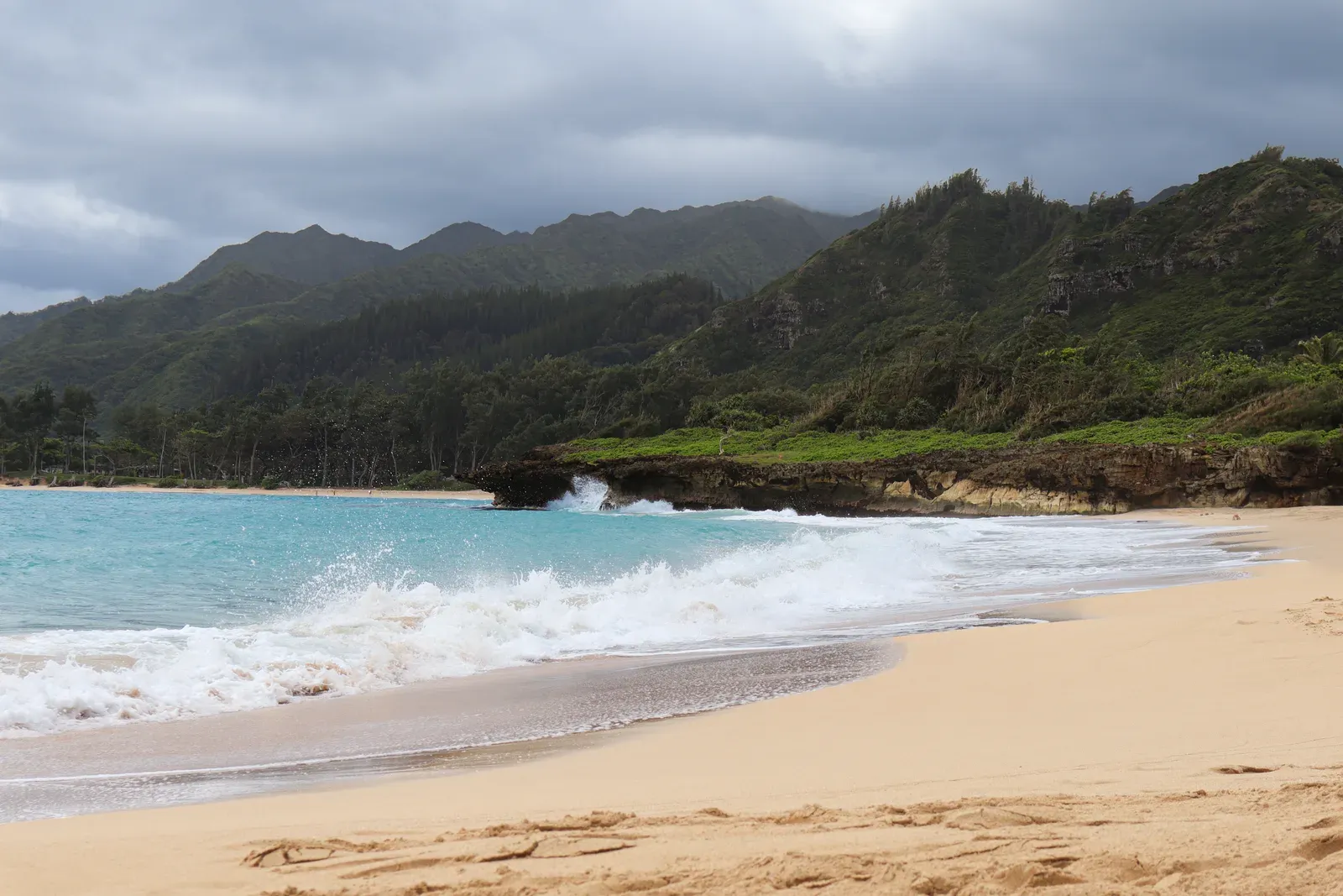 Waves on a sandy beach with green mountains behind.